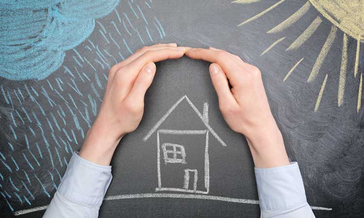 hands protecting a chalk drawn house from the elements on a blackboard
