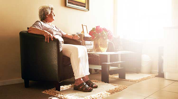 older lady sitting in a chair and looking out of a sunlit window