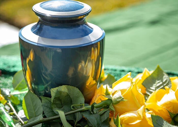 a shiny urn next to yellow flowers with sunshine in the background