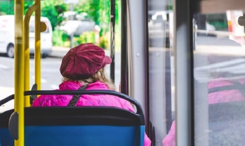 Woman sat on bus wearing a pink coat and gazing out window