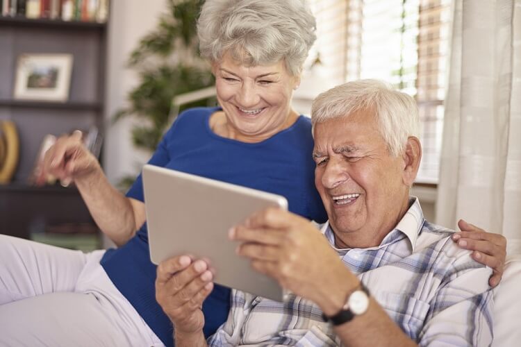 Older woman and man sitting together laughing and reading a tablet