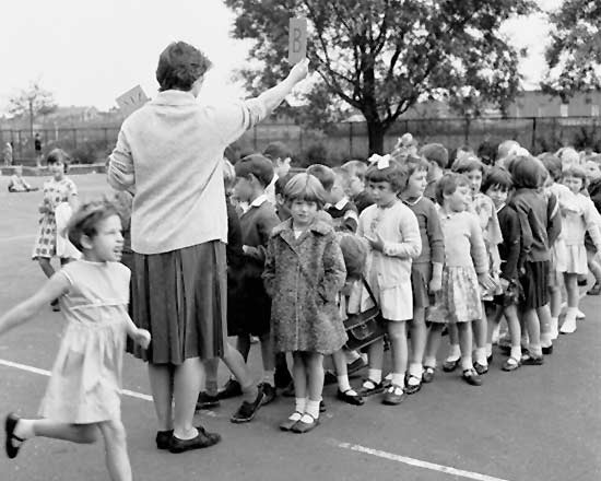 Children lined up in front of a teacher in the playground