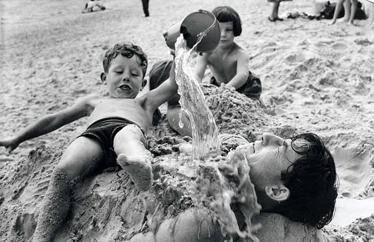 A young boy pouring a bucket of water over his dad