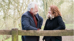Retired couple leaning on a fence in the woods
