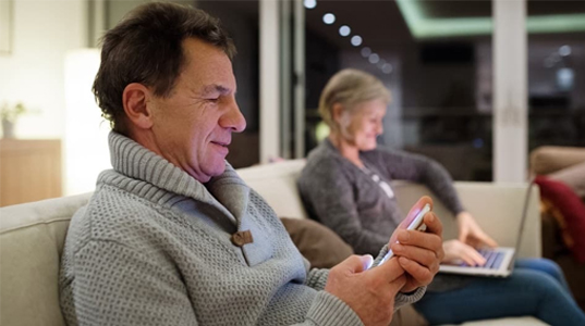 Older couple on a sofa looking at devices.